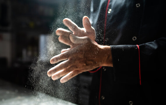 Chef clapping flour off hands in dramatic kitchen light