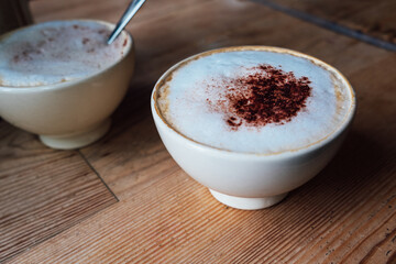 Cup of freshly made delicious cappuccino coffee with fluffy foam and cacao powder on rustic wooden background in modern bar.