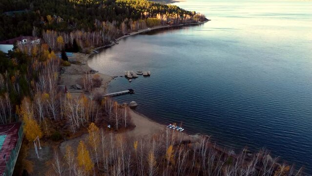 Gentle autumn rays illuminate the picturesque Shchuchye Lake with a cozy pier surrounded by a forest of birch and pine trees. Aerial footage from a drone. Kazakhstan