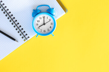 Blue alarm clock and notepad on a yellow background, flat design.