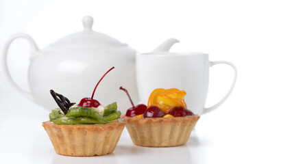 Colorful fruit cakes made with kiwi, orange, candied cherry, cream and chocolate isolated on a white background with a cup and a teapot.