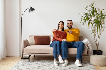 Relaxed young couple sitting on sofa, watching tv at home