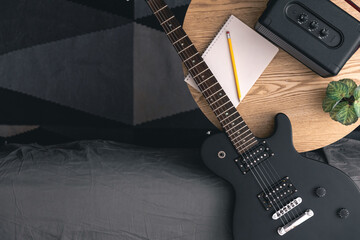 Electric guitar, notepad and music speaker on a table in the room, top view. - obrazy, fototapety, plakaty
