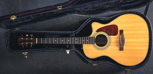 Acoustic guitar in a protective case on a dark background, top view.
