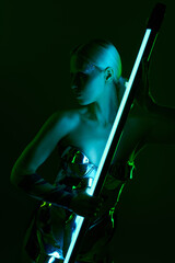 extraordinary woman in metallic robotic attire holding blue LED lamp stick and looking away