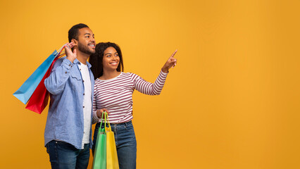 Nice Offer. Excited young black spouses with bright shopping bags pointing aside