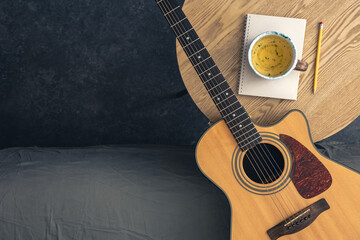 Musical background with acoustic guitar, notepad and cup of tea on the table.