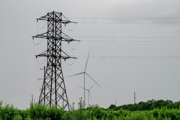 Power distribution lines connected to transmission tower on windfarm. Wind turbines with rotor...