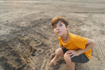 Portrait of a boy in nature. A boy in an orange T-shirt plays with mud in the ground in nature. Happy child, lifestyle. Candid Portraits.