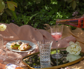 Spring refreshment drinks. Light pink rose cocktail lemonade on picnic in blossom garden with blurry natural green backgound