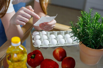 Woman Checking Bills In Kitchen After Grocery Shopping, At Table In Kitchen, Closeup Shot, Selective Focus