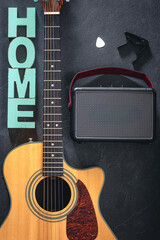Acoustic guitar, speaker and word Home on a black background, top view.