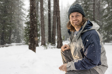 Obraz premium A man wearing a blue and gray jacket and a black hat is smiling in the snow. He is sitting on the ground and he is enjoying the winter weather