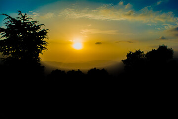 Fototapeta premium Sunset view from the mountains of Lansdowne. Mountain Sunset view in Lansdowne. Amazing golden sunset seen through forest drive, Lansdowne Uttarakhand.