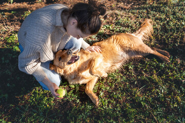 Young happy charming girl playing with her retriever dog with a ball on green grass. - 751563262