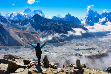 A Trekker celebrates reaching the summit of 5350 m high Gokyo Ri providing grand stand views of the Highest mountain peaks on Earth - Everest,Lhotse,Makalu, Cho Oyu and the Ngozumpa glacier in Nepal - obrazy, fototapety, plakaty
