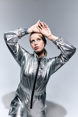 fancy female model in silver unusual attire posing in motion on gray backdrop and looking away