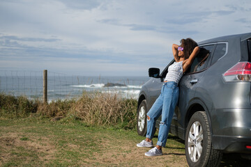 Relaxed and blissful young black woman leaning on her car in front of the sea. Getaway to take a break and enjoy the outdoors and freedom.