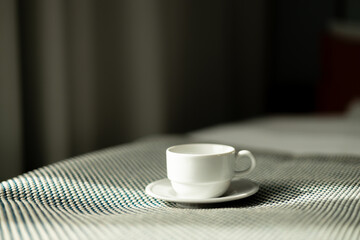 Coffee or tea cup on the bed. Hotel room or bedroom Interior, morning time. Concept of easy breakfast. One white ceramic cup.