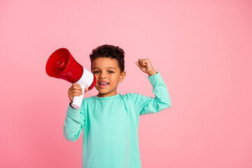 Photo portrait of cute little boy winning raise fist hold megaphone dressed stylish cyan clothes isolated on pink color background