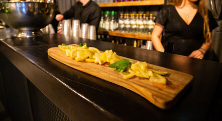 Sliced fresh lemons artistically presented on a wooden board in a bar setting, with bartenders in...