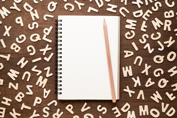 Empty notebook and pencil with many English alphabets around on the table, word choices for create writing, imagination for starting the story concept