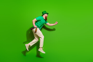 Full length profile portrait of overjoyed guy jump rush hold beer bottle empty space isolated on green color background
