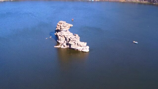 Aerial drone footage of the stone island of Zhumbaktas in the middle of Lake Borovoe, people strolling on catamarans and boats. National park Burabay Borovoe , Kazakhstan