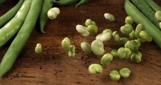 Super slow motion close up of fresh raw organic vegetable garden unshelled fava broad beans are falling for quality control on rustic wooden table in rural agriculture farmland at 1000 fps.