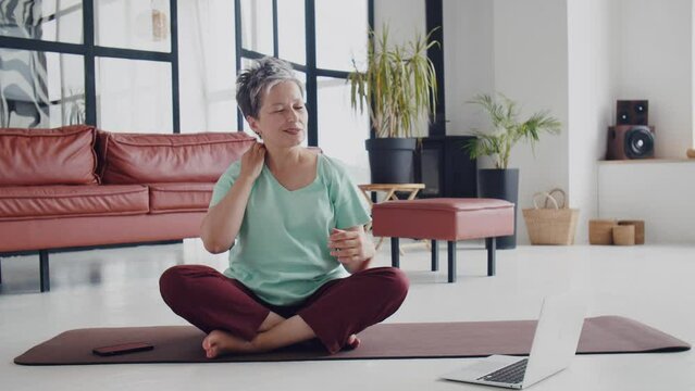 Old woman make yoga exercise at home. Mature woman preparing to exercise by warm up muscle, neck, hands, head