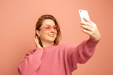 Cheerful funny woman 40s wearing casual sweater posing doing selfie shot on mobile phone over pink...