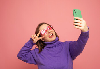 Cheerful funny woman 40s wearing casual sweater posing doing selfie shot on mobile phone over pink...
