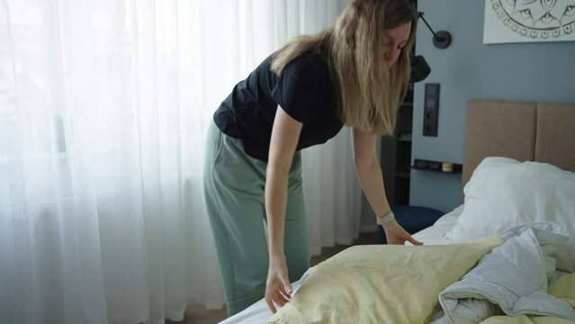 Woman replacing bed linen in room. Female making bed in bedroom. Routine chores and housework
