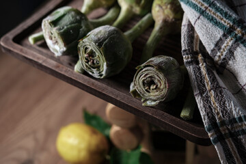 fresh frozen baby artichoke buds raw on kitchen cloth textle, wooden board, dark rustic colors, ready to cook