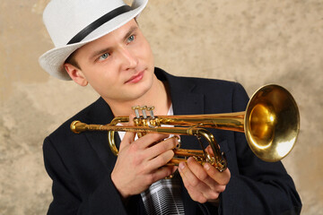 Young handsome man in white hat and jacket poses with trumpet in studio