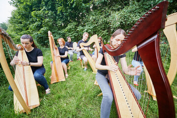 Ensemble of seven musicians play harps outdoors