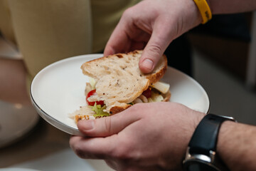 Person eating food, a hand holding sandwich on plate