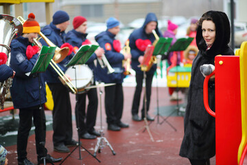 Brass band of six musicians play on playground and women poses at winter day, focus on woman