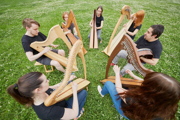 Ensemble of seven musicians play celtic harps performing outdoors at grassy lawn
