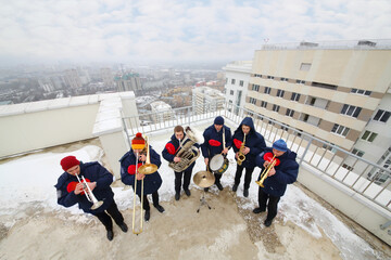 Brass band of six musicians play on roof of tall building at winter, top view