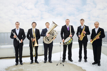 Brass band of six musicians pose on roof of tall building at winter