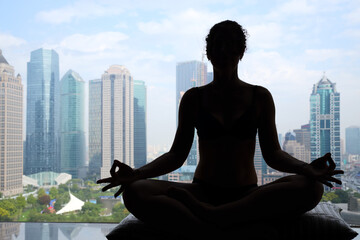 Woman in underwear meditates on windowsill with view of skyscrapers