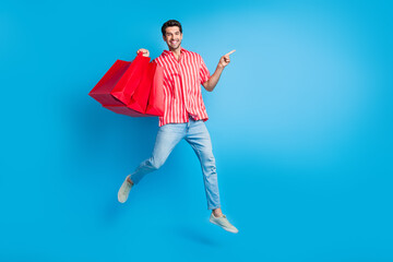 Full size photo of optimistic man dressed striped shirt fly hold new clothes directing empty space...