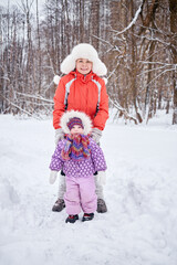 Mother with little daughter stand in snowy winter park