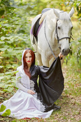 Young woman in black and white dress sits near horse in park