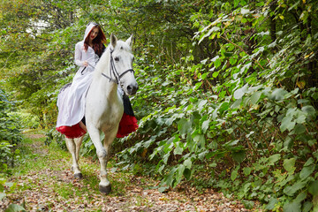 Young woman in black and white dress rides on horseback in park