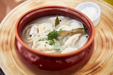 Ceramic pot with boiled pelmeni and bowl with sauce.