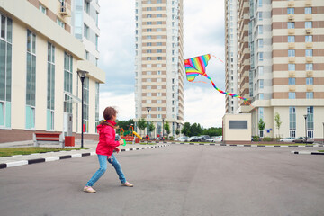 Girl in red jacket and blue jeans let kite on local area of high-rise buildings