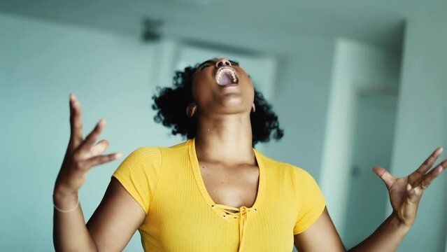 One desperate young black woman screaming in furious outrage feeling overwhelmed and stressed out by pressure, 20s person gesticulating arms feeling extreme anger
