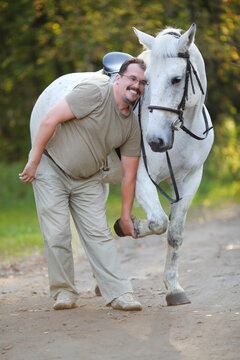 Happy man plays with beautiful white horse in sunny autumn park